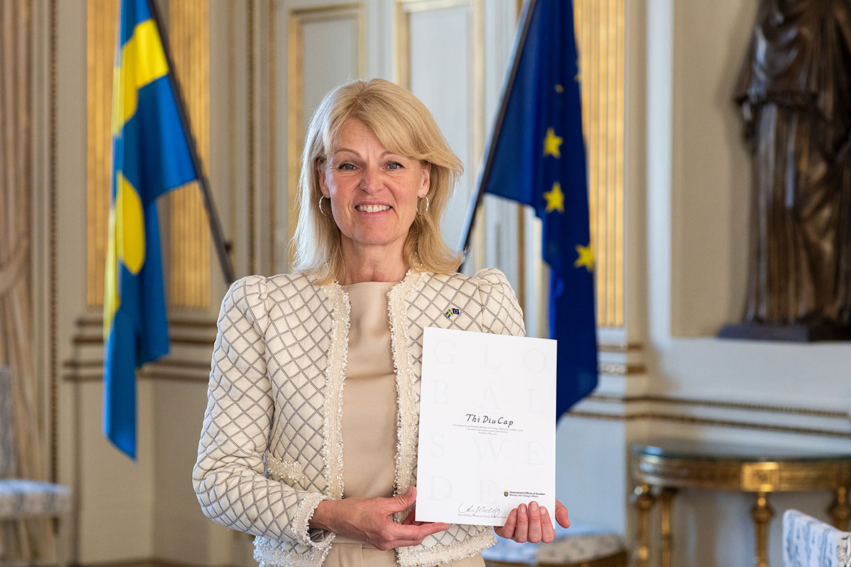 Kvinna håller upp diplom. I bakgrunden hänger svenska flaggan och EU-flaggan.