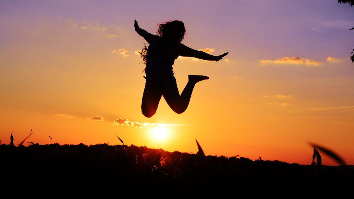 Student som hoppar på en äng i solnedgången