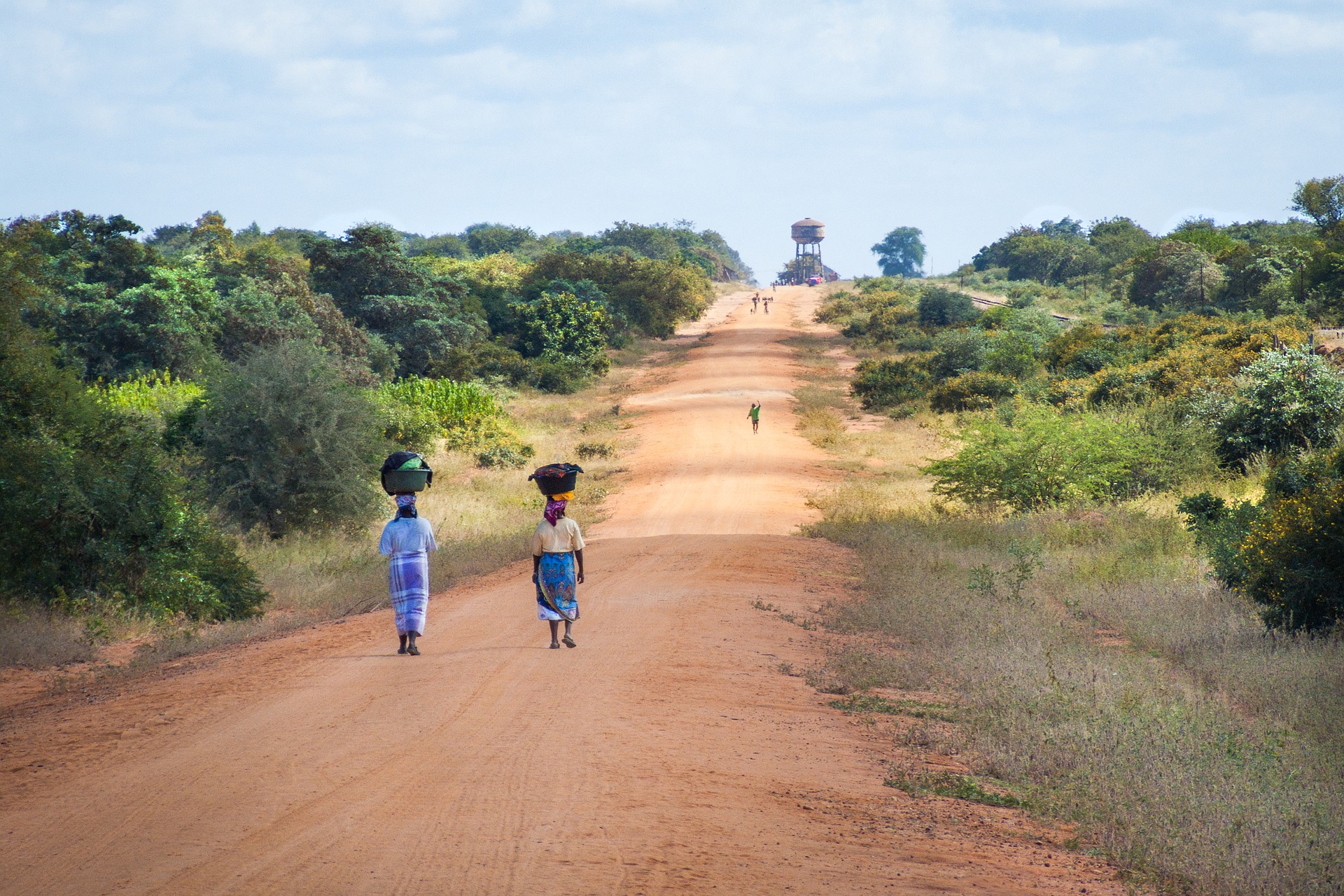 Oasfalterad väg på landsbygden i Moçambique. Två kvinnor går längs med vägen med korgar på huvudet.